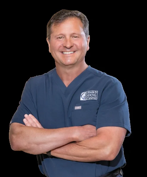Dr. Michael Kirk in Grand Dental Studio scrubs, arms folded, smiling.